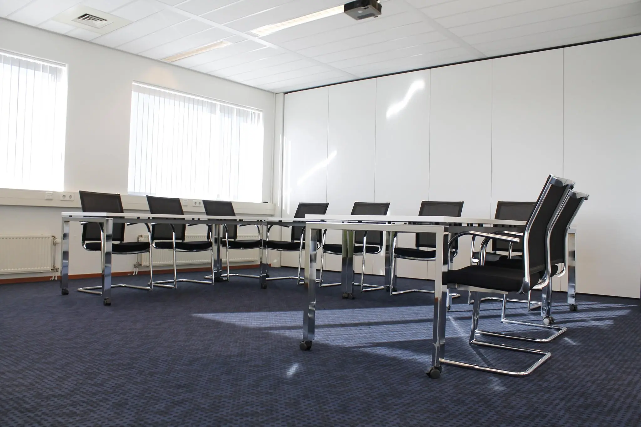 Vergaderruimte aan de Laan van ’s-Gravenmade met moderne meubels, blauwe vloerbedekking en ramen met verticale jaloezieën.